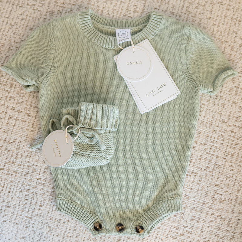Green baby onesie with matching knit baby booties on a textured surface