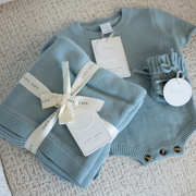 Blue baby knit sweater onesie with matching baby blanket and booties on a textured surface