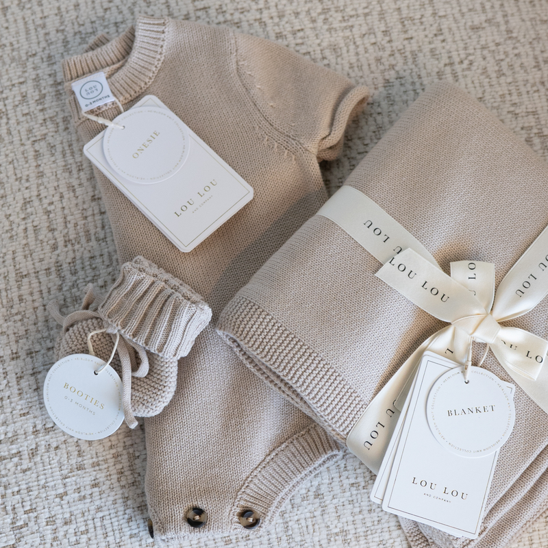 Tan baby outfit with matching booties and blanket on a textured surface with 'LOU LOU' branding.