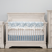 A white traditional-style wooden crib with a blue and white padded rail cover.