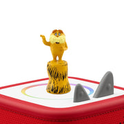 A red square electronic device with a white top panel, featuring a small yellow cartoon lion figure standing on a textured yellow pedestal and two gray shark-shaped elements on the surface, shown against a plain white background.