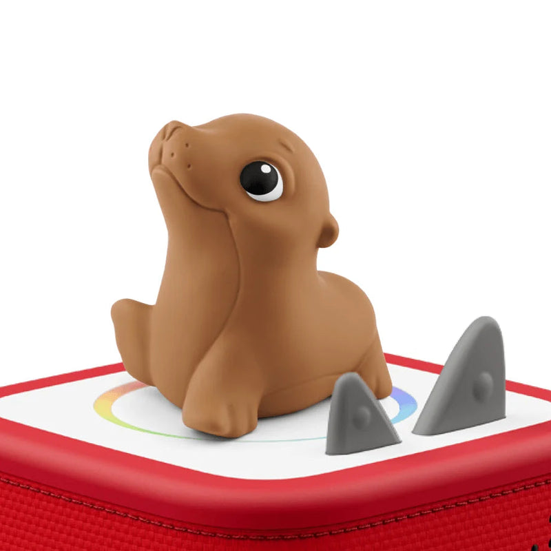 A small brown seal toy sitting on top of a red and white square device with two gray shark-shaped accents, isolated on a white background.