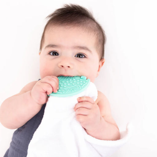 Baby holding a green and white teething toy against a white background