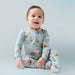 Smiling baby sitting upright wearing the same football-print romper against a soft blue backdrop.