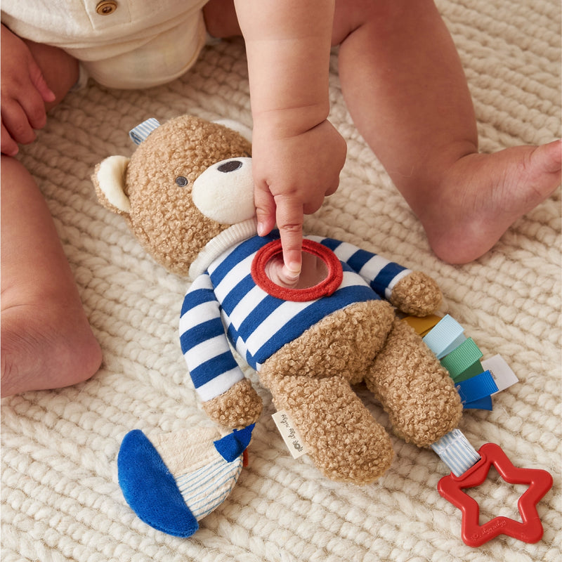 Close-up of baby hands interacting with the Bitzy Traveler toy, showing dangling ring and soft textures