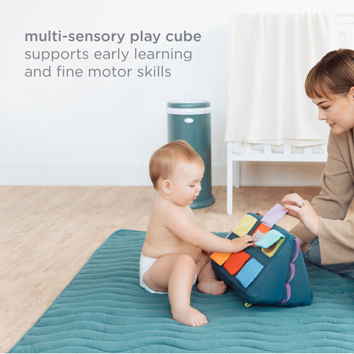 Baby sitting on a play mat interacting with the Ubbi multisensory mirror activity toy during floor play