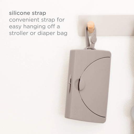 Ubbi On-the-Go Wipes Dispenser hanging from a hook by its silicone strap, which attaches to a stroller or diaper bag