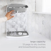 Hand placing a bottle on the Ubbi Vertical Bottle Drying Rack, which has 13 pegs for bottles and pump parts