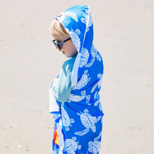 Child wearing a blue hoodie with turtle pattern on a sandy background