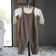Brown knitted overalls on a hanger with a white shirt underneath, against a neutral background.