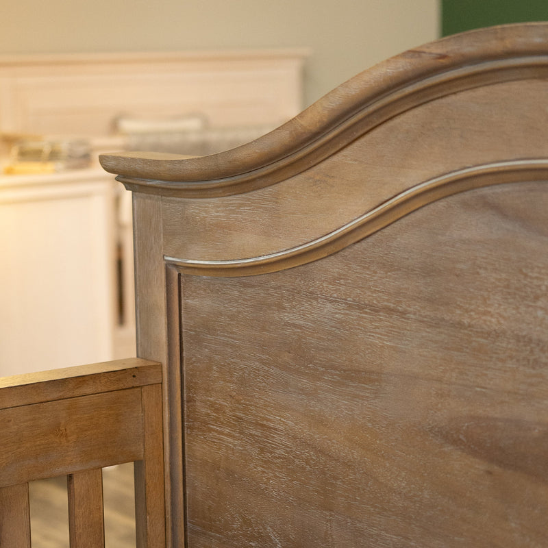 Wooden headboard of an arch top crib in a baby nursery