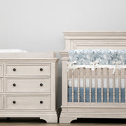 White nursery furniture set with crib and dresser against a light gray wall.