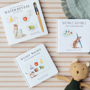 Three children's books on a striped surface with a plush toy and blanket.