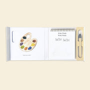 Open book with paint palette illustration and pen on beige background