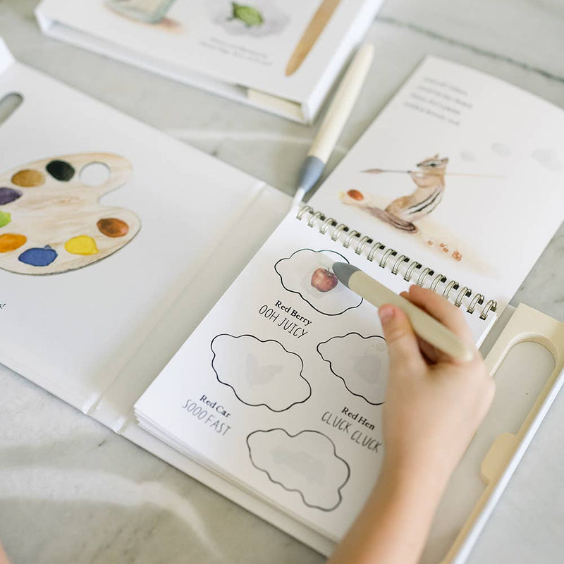 Open book with coloring pages and a hand holding a pen on a light surface.