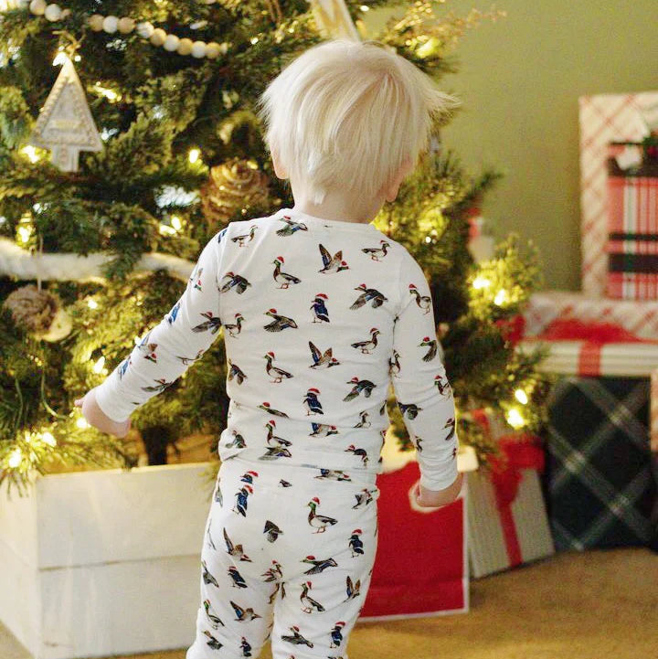 Child wearing Saltwater Swaddles Duck the Halls pajamas standing near Christmas tree in festive room