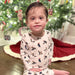 Child sitting in front of Christmas tree wearing Saltwater Swaddles Duck the Halls pajamas with holiday duck print