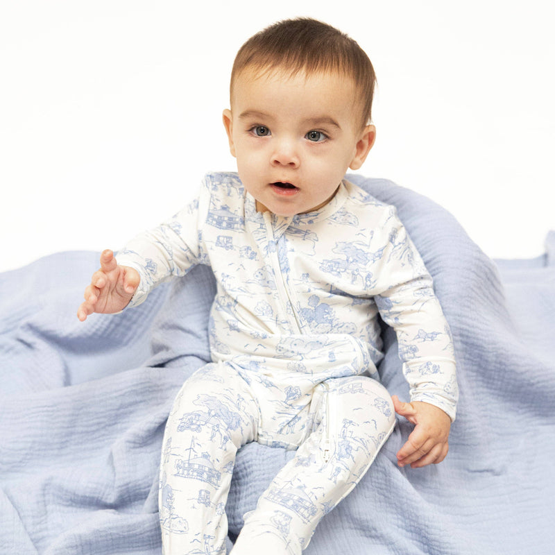 Baby wearing a white onesie with blue patterns sitting on a blue blanket.
