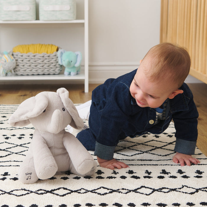 Baby crawling toward Flappy the Elephant plush on a nursery rug