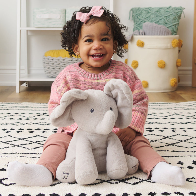 Toddler sitting on a rug smiling with Flappy the Elephant plush