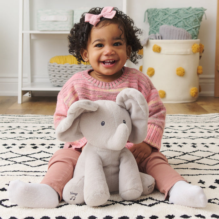 Toddler sitting on a rug smiling with Flappy the Elephant plush