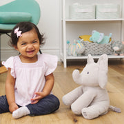 Baby seated on the floor beside Flappy the Elephant plush